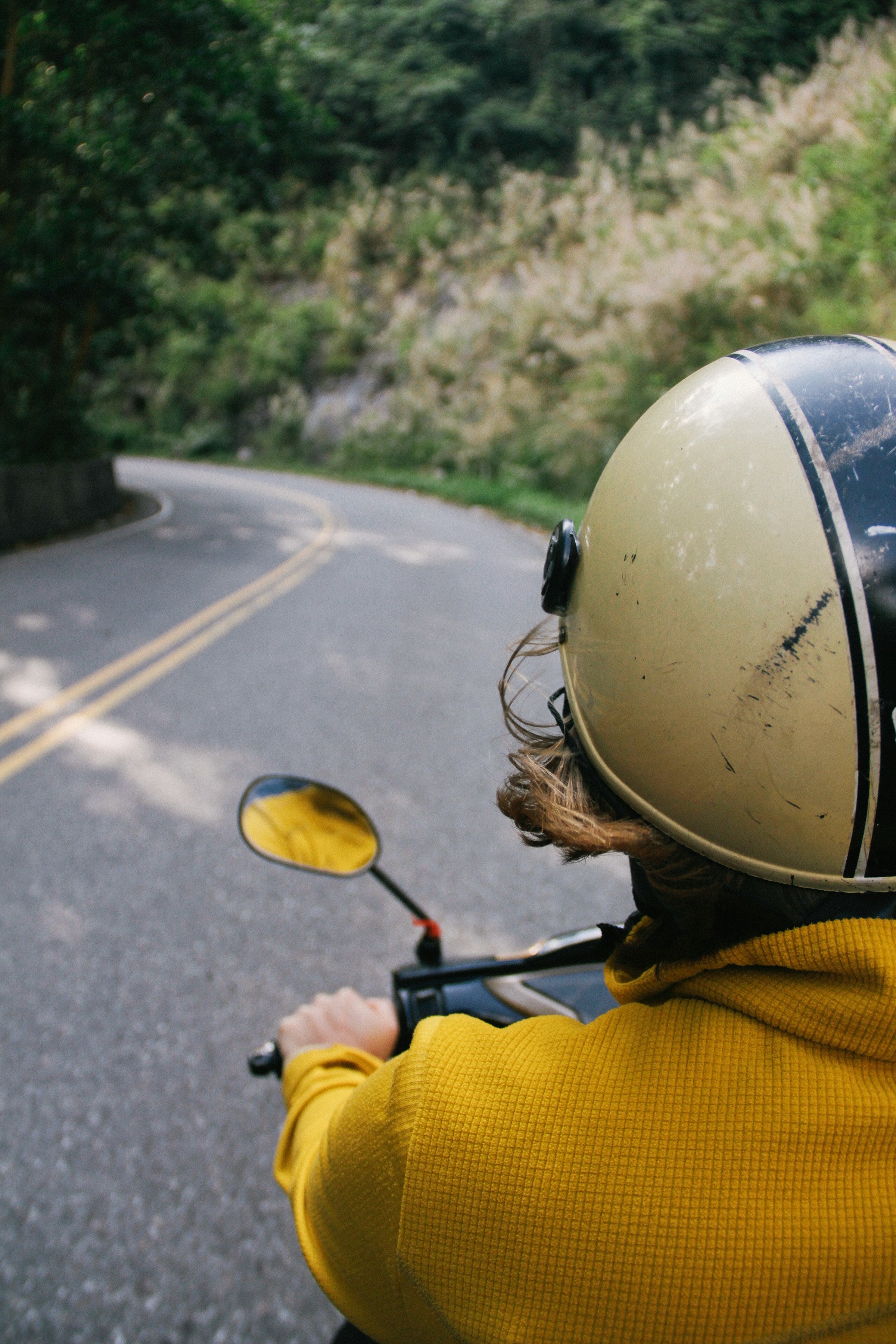 Person wearing a helmet and yellow jacket on a motorcycle with a scenic road in the background
