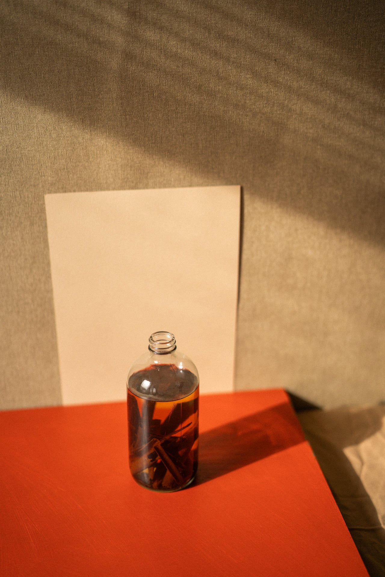 Clear bottle with dark liquid on a red surface against a textured beige wall