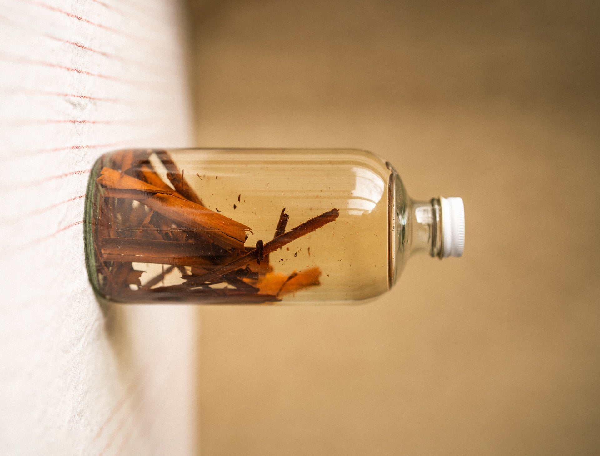 Clear glass bottle with cinnamon sticks and orange peels on a neutral background